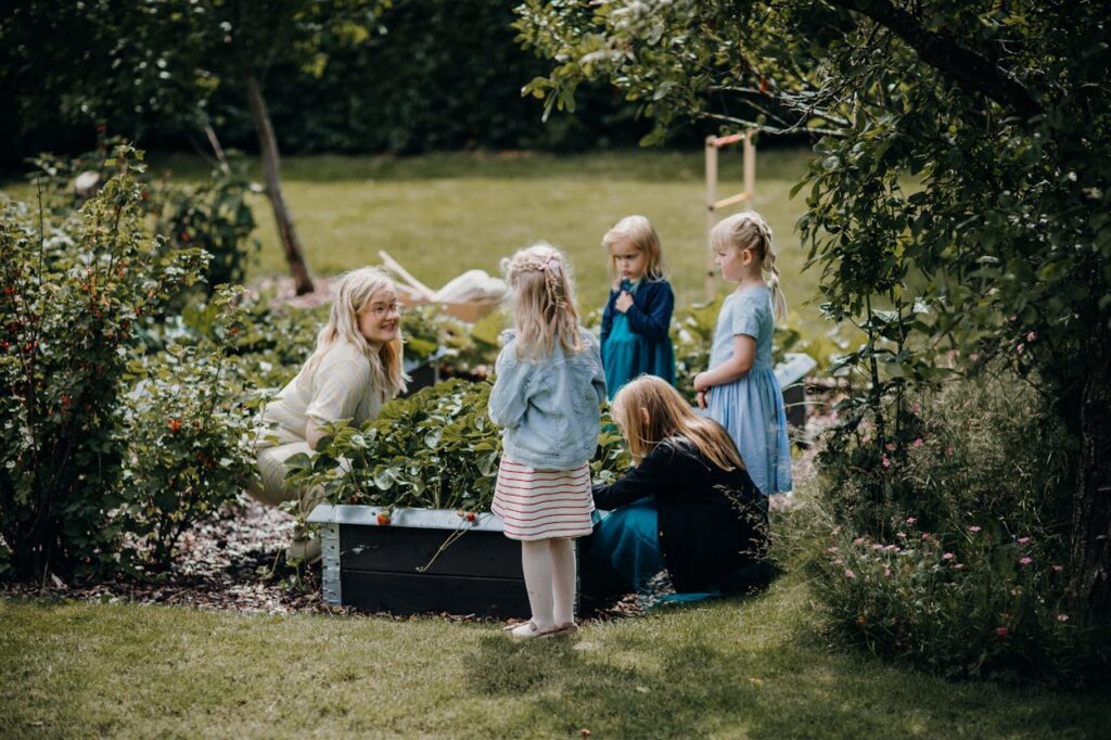 A group of children and an adult gardening together in a lush, green backyard setting, enjoying outdoor activities.